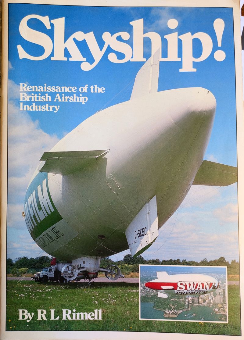 Picture of book cover showing rear view of a branded airship moored to vehicle on the ground with a small picture of a branded airship flying above a bay adjacent to a city skyline.